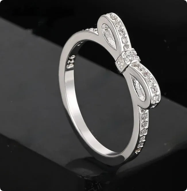 Silver electroplated bow ring with sparkling zircon crystals on a finger.