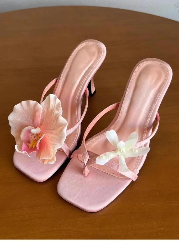 Women's black asymmetric floral high-heel sandals with a square toe and calf leather upper.