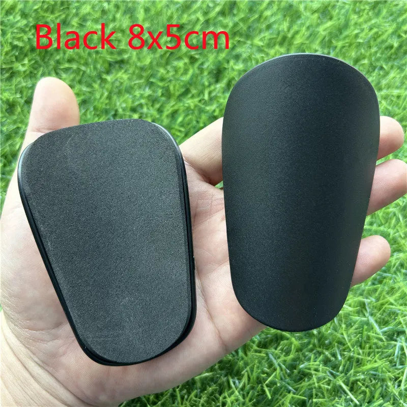 Pair of extra small black and white plastic football shin guards, measuring 8cm by 5cm.