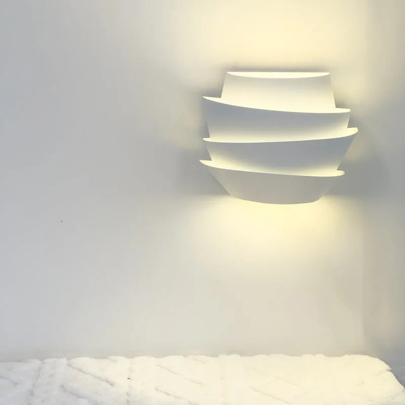 Modern white wall lamp with pine cone decoration mounted on a plain wall.
