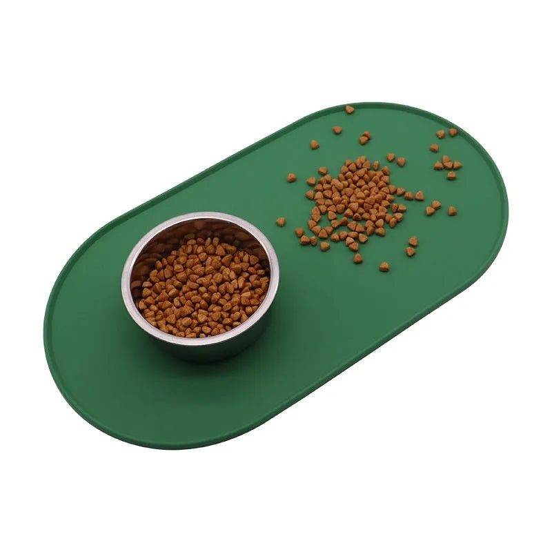 Green silicone cat feeding placemat on a floor next to a food bowl.