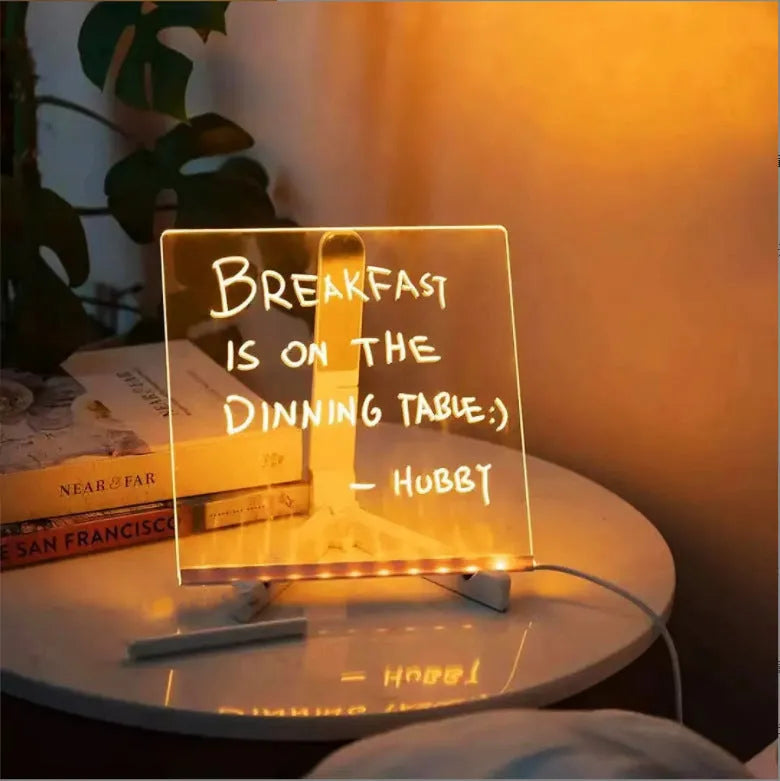 DIY acrylic LED message board lamp on a desk with colourful writing, showing USB cable and pens.