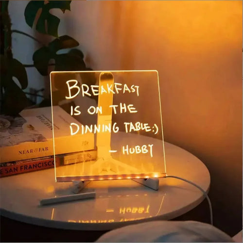 DIY acrylic LED message board lamp on a desk with colourful writing, showing USB cable and pens.