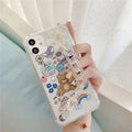 White iPhone case with a bear cartoon design and a silver chain with a bear pendant attached.