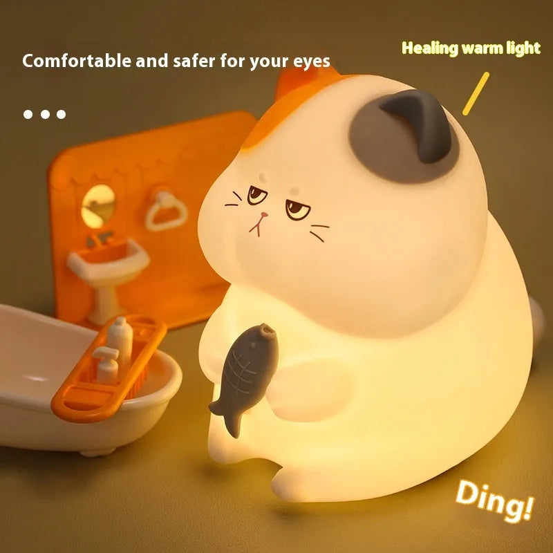 Small yellow Greedy Cat cartoon night light on a desktop, showing fish theme and compact size.