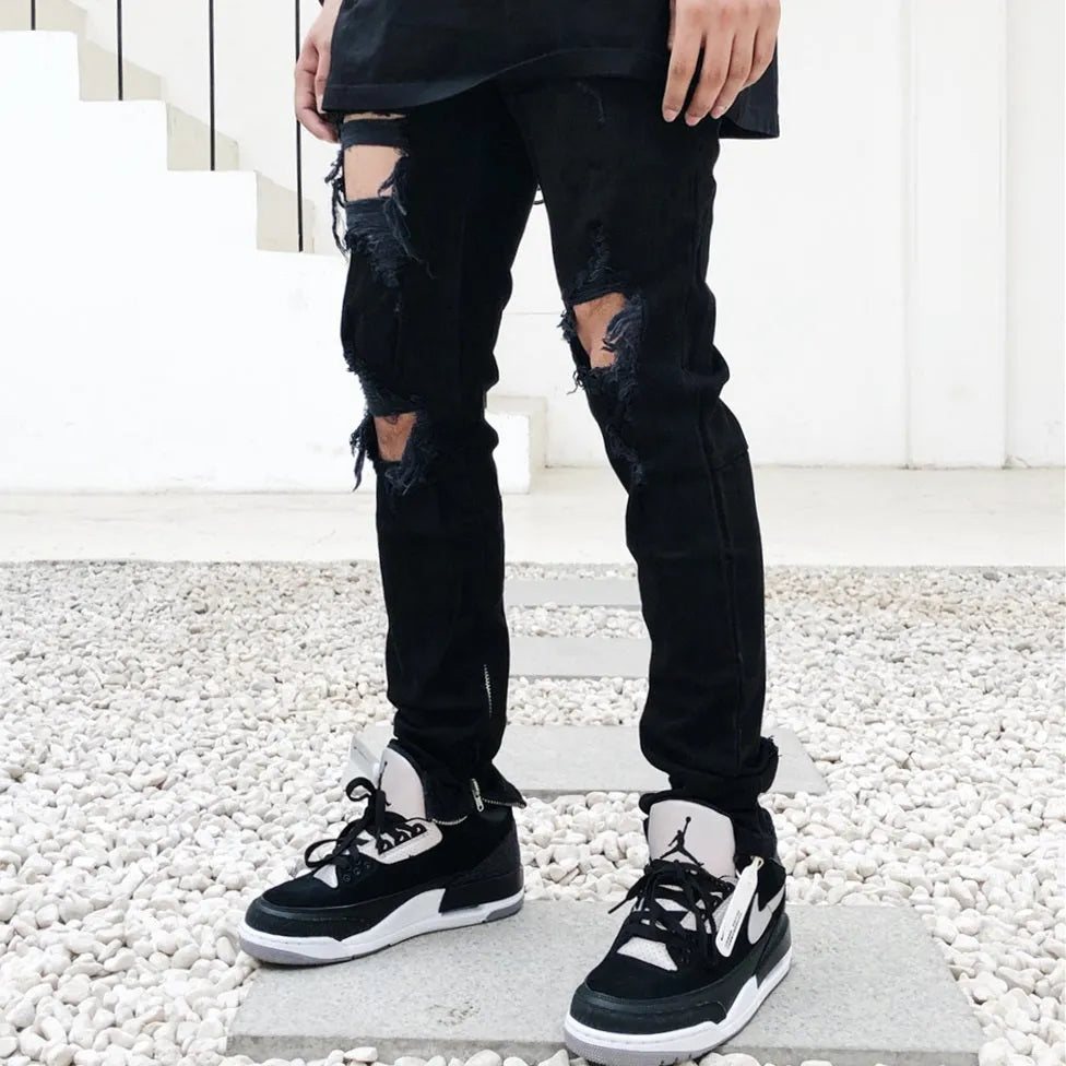 Men's high street style black torn jeans in washed black denim with raw edge details, front view.