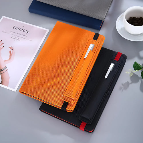 A5 faux leather notebook with pen insert and strap, open on a desk showing lined pages