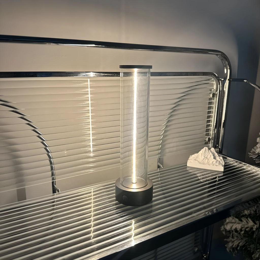Tall cylindrical frosted glass USB rechargeable LED night light with a magnetic base on a wooden surface.