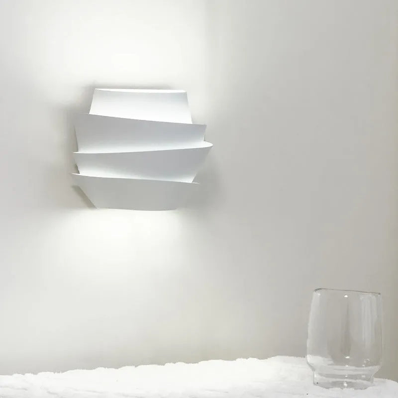 Modern white wall lamp with pine cone decoration mounted on a plain wall.