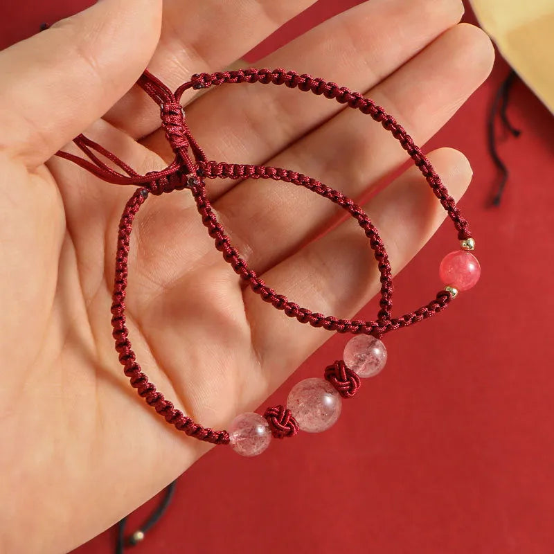 Woven red rope bracelet with a spherical strawberry quartz bead and alloy clasp.