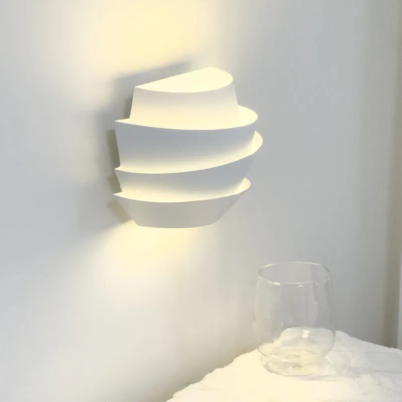 Modern white wall lamp with pine cone decoration mounted on a plain wall.