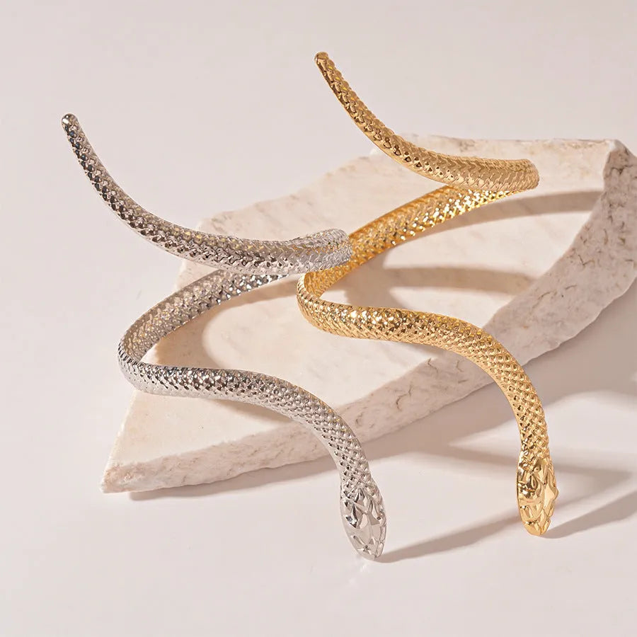 Gold exaggerated twisted snake design bracelet and ring jewellery set on a dark background.