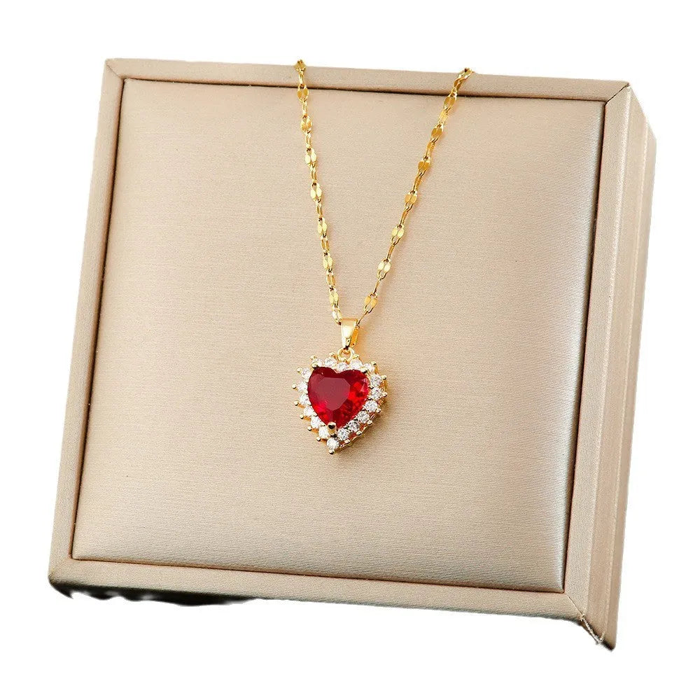 Gold red titanium steel necklace with heart and flower gemstone pendant, matching earrings, and ring on a grey background.