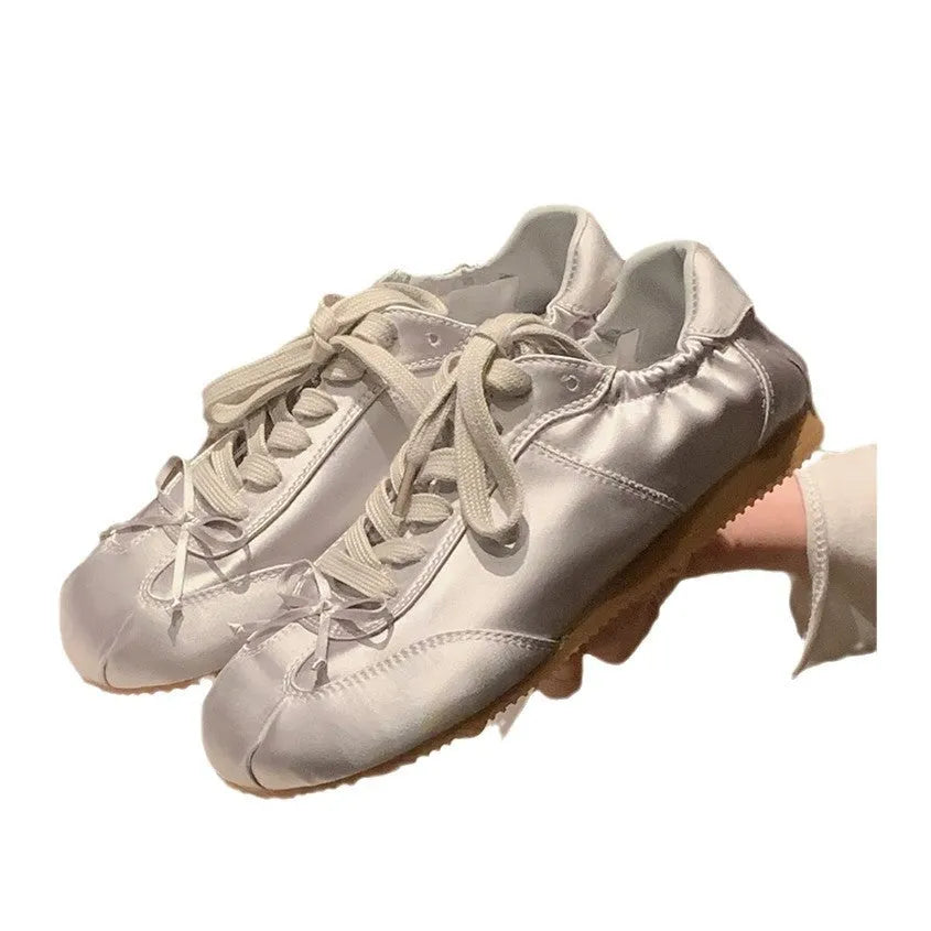 Women's champagne pink satin ballet flats with round toe and lace-up front, shown on a white background.