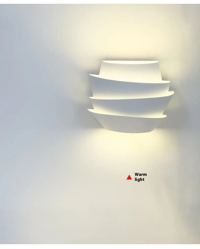 Modern white wall lamp with pine cone decoration mounted on a plain wall.