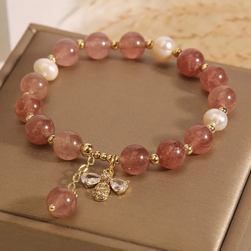 Adjustable pink strawberry quartz bracelet with three freshwater pearls and sparkling zircon charms on a wrist.