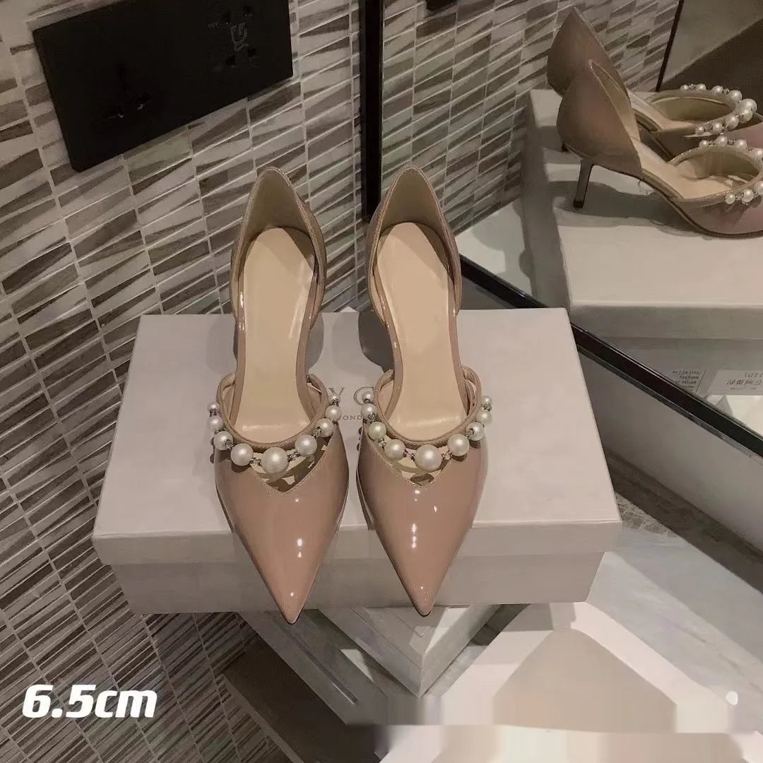 Women's black patent leather stiletto high heels with pointed toe and pearl decoration on display.