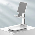 White folding telescopic mobile phone bracket holding a smartphone on a desktop.
