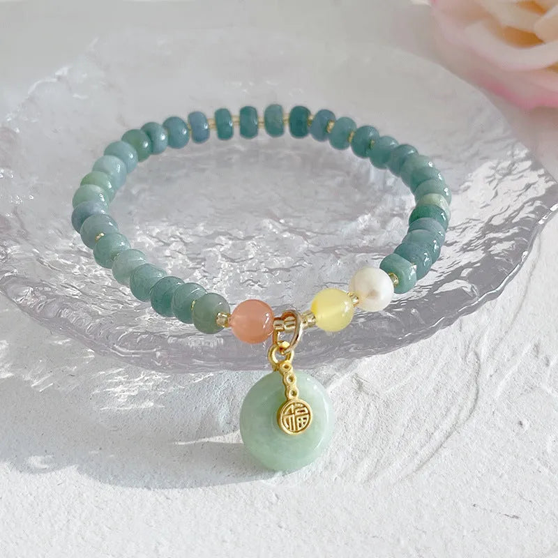 Close-up of a blue jade women's bracelet showing a gourd charm and a peace buckle charm on a string.