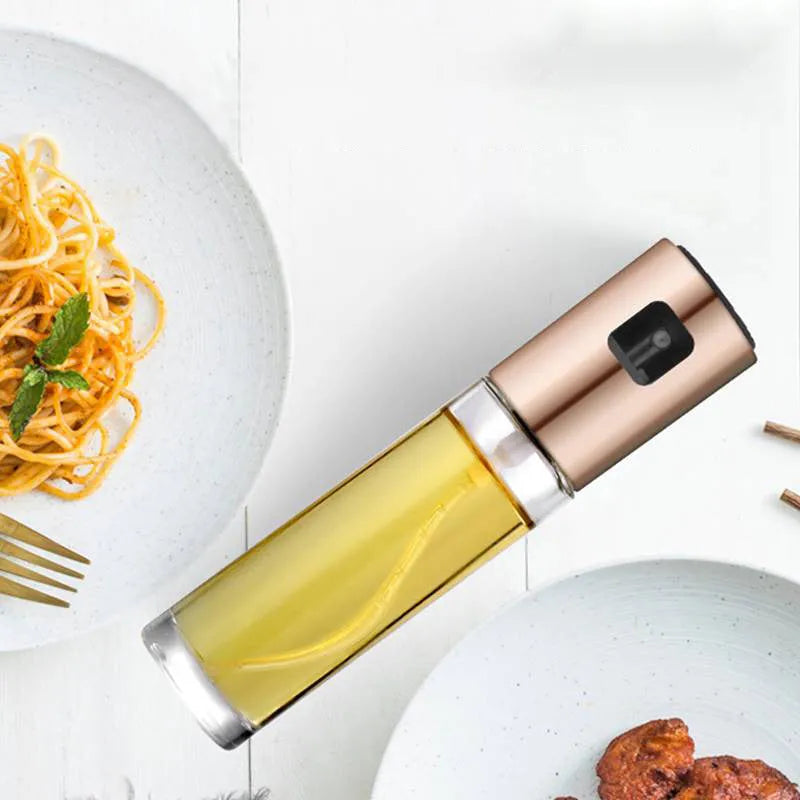 Gold pump-action oil and vinegar spray bottle with 100ml glass body on kitchen counter.