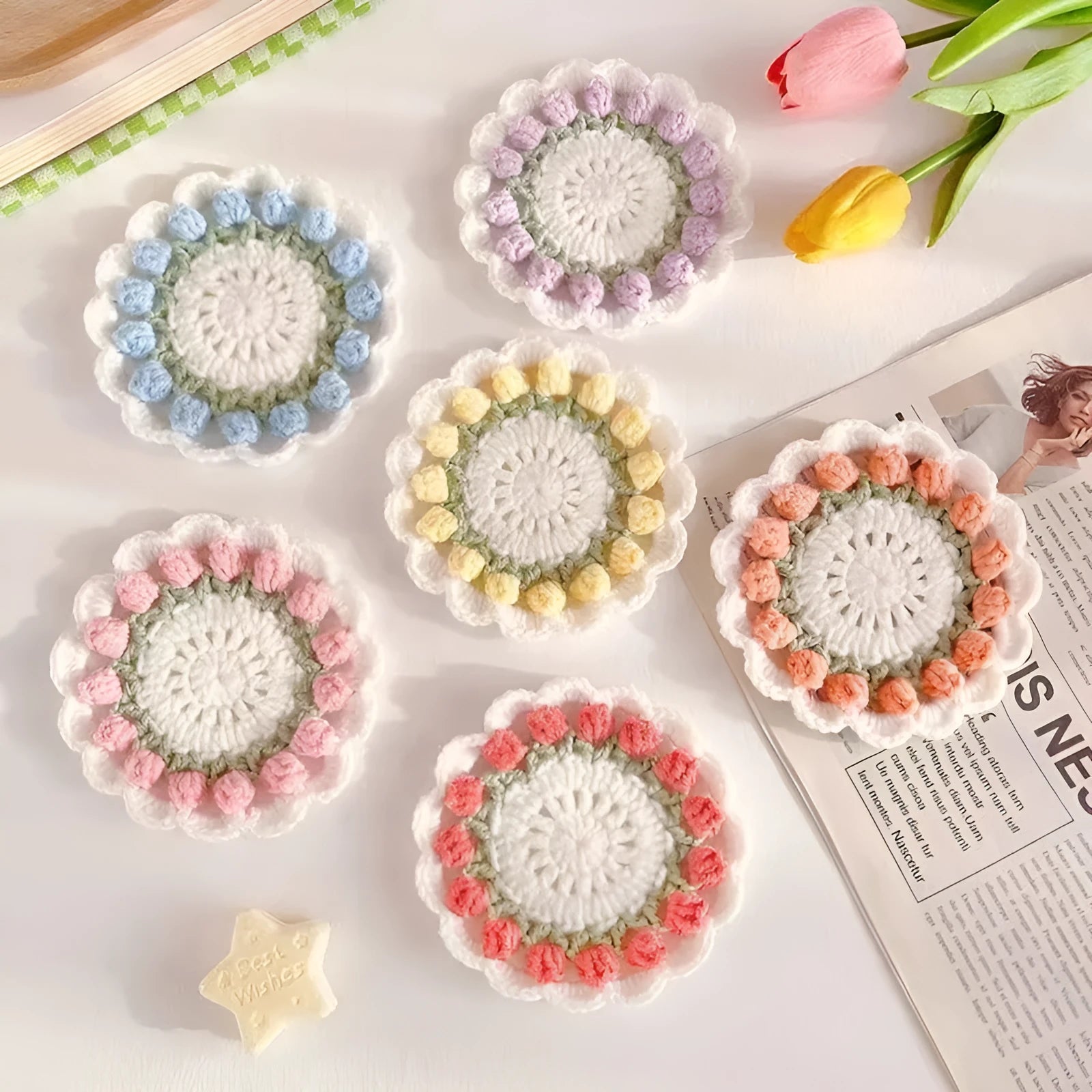 Set of four handmade woven floral coasters in pink, purple, red, and yellow on a wooden table.