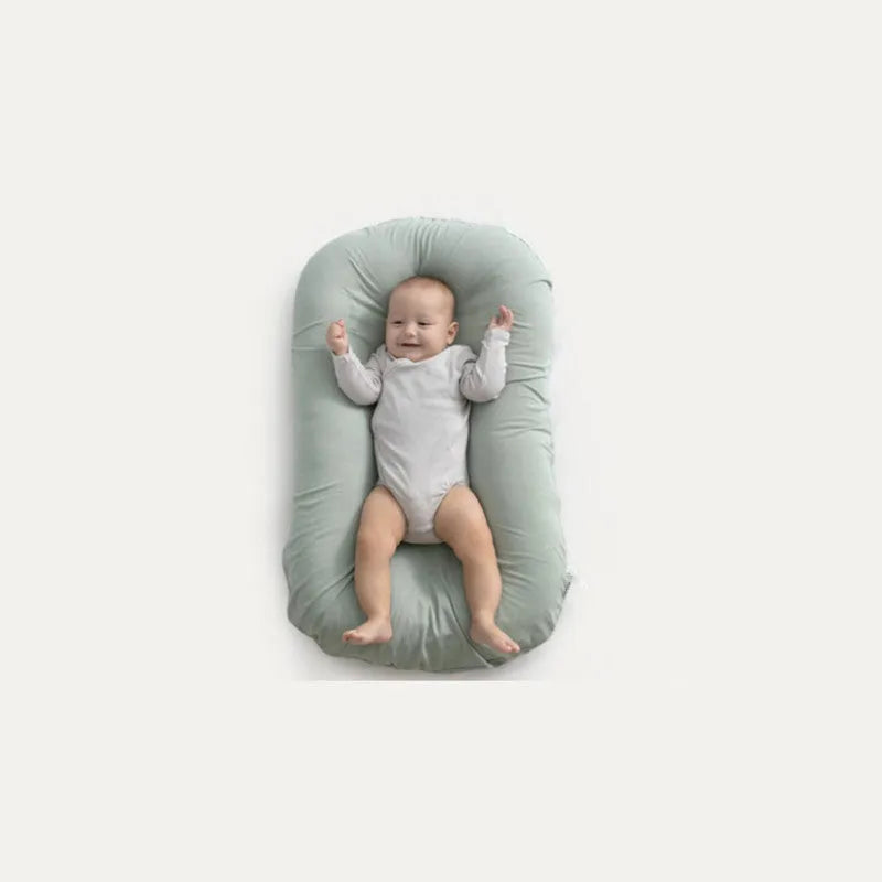 Cotton portable baby nest crib for newborns, beige colour, shown on a bed.