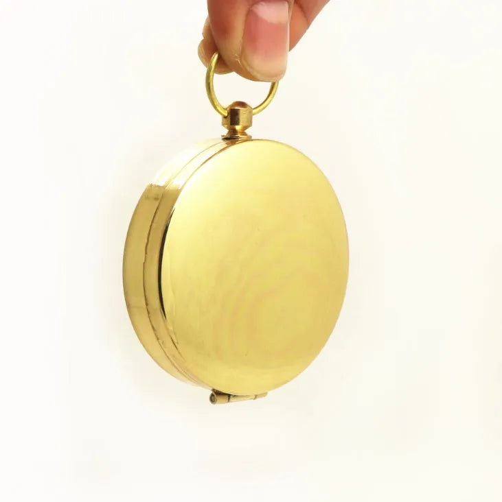 Gold metal flip compass with open lid showing compass face, pocket watch style