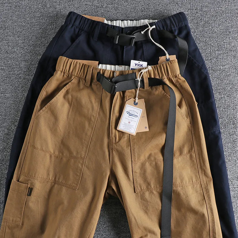 Man wearing khaki cotton work trousers with a buckle belt and structured three-dimensional cut.