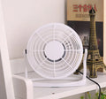 Small black USB desk fan with adjustable tilt on a wooden desk next to a laptop