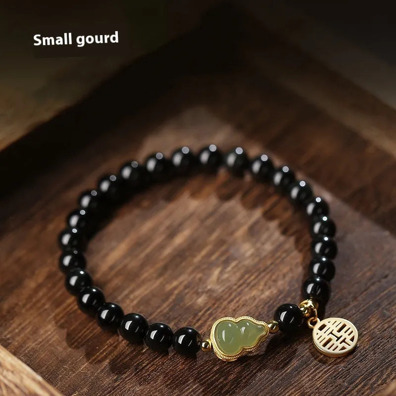 Black obsidian bead bracelet with a carved Hetian jade gourd charm, shown in geometric retro style.
