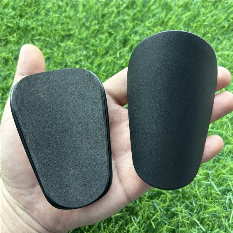 Pair of extra small black and white plastic football shin guards, measuring 8cm by 5cm.
