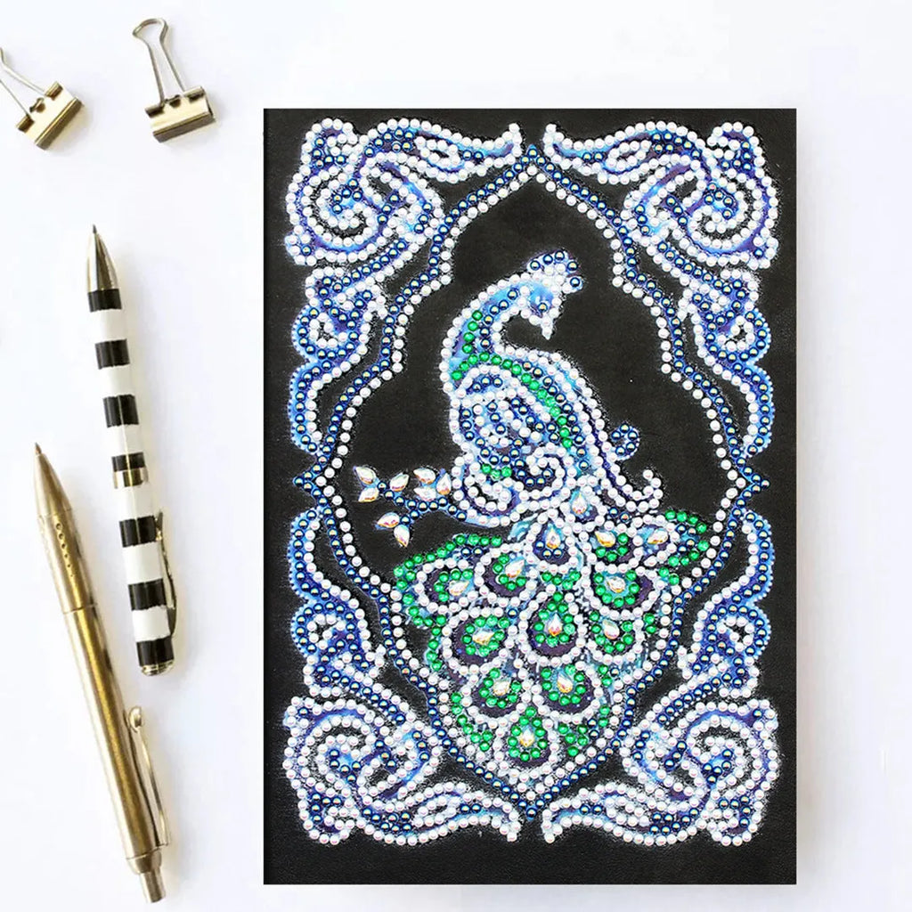 A5 black notebook with a peacock diamond painting design and packets of shaped and bright drill rhinestones.
