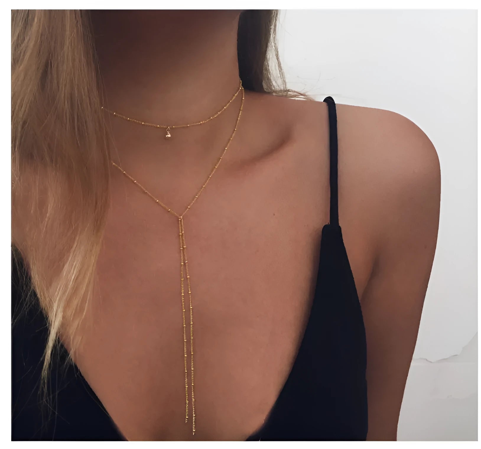 Multilayer lariat necklace in gold with three alloy chains on a plain background