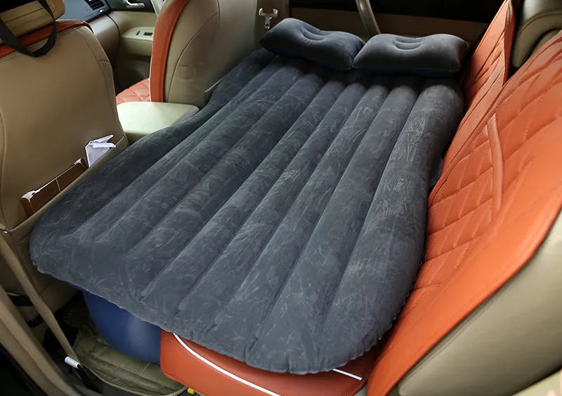 Black inflatable car bed with flocked surface, shown with storage bag and pillows, ready for use in a vehicle.