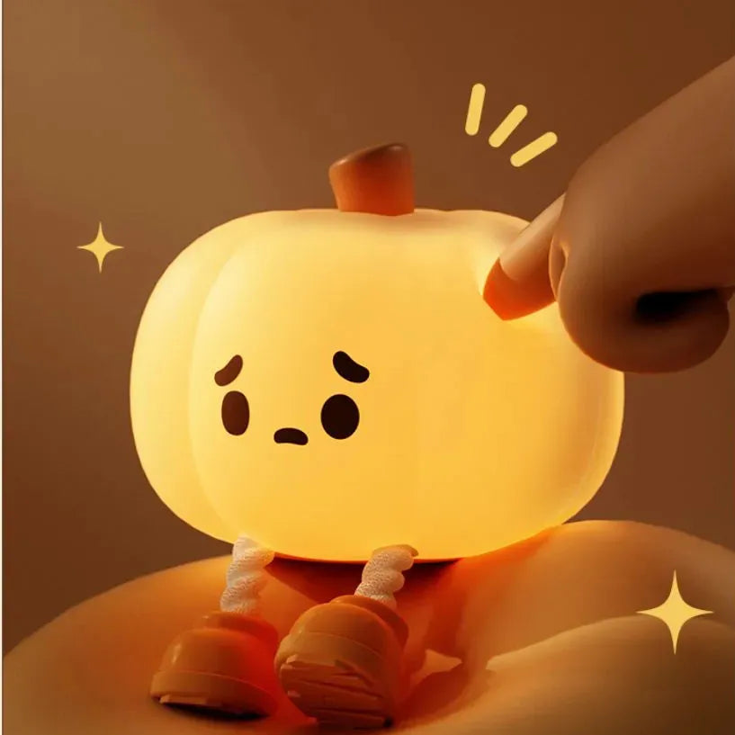 Soft orange pumpkin-shaped silicone night light with a warm glow, showing its compact size on a table.