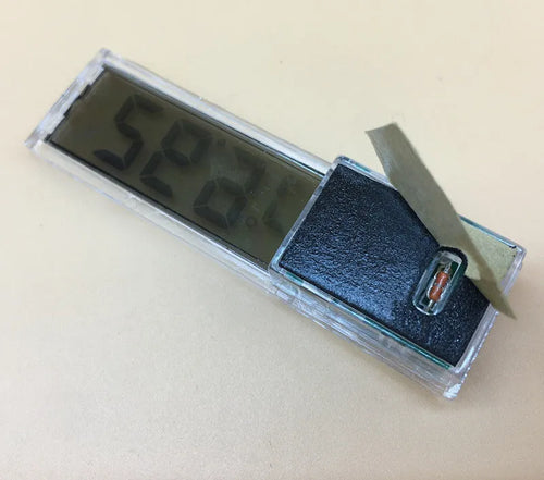 Gold digital thermometer mounted on aquarium glass showing temperature reading
