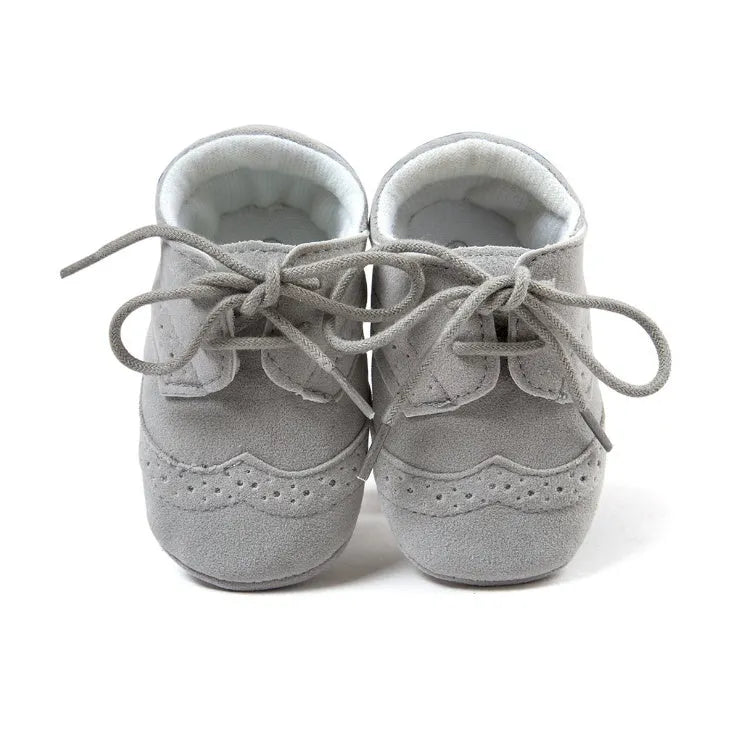 Vintage-style soft-soled baby shoes in black, grey, light brown, and white for infants 0-12 months.
