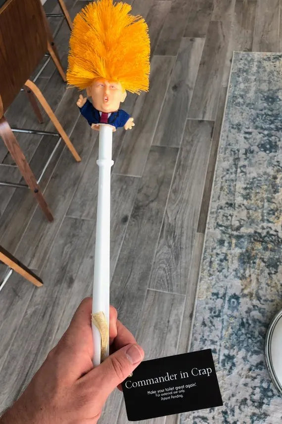 Yellow plastic Donald Trump toilet brush with hanging slot on handle.