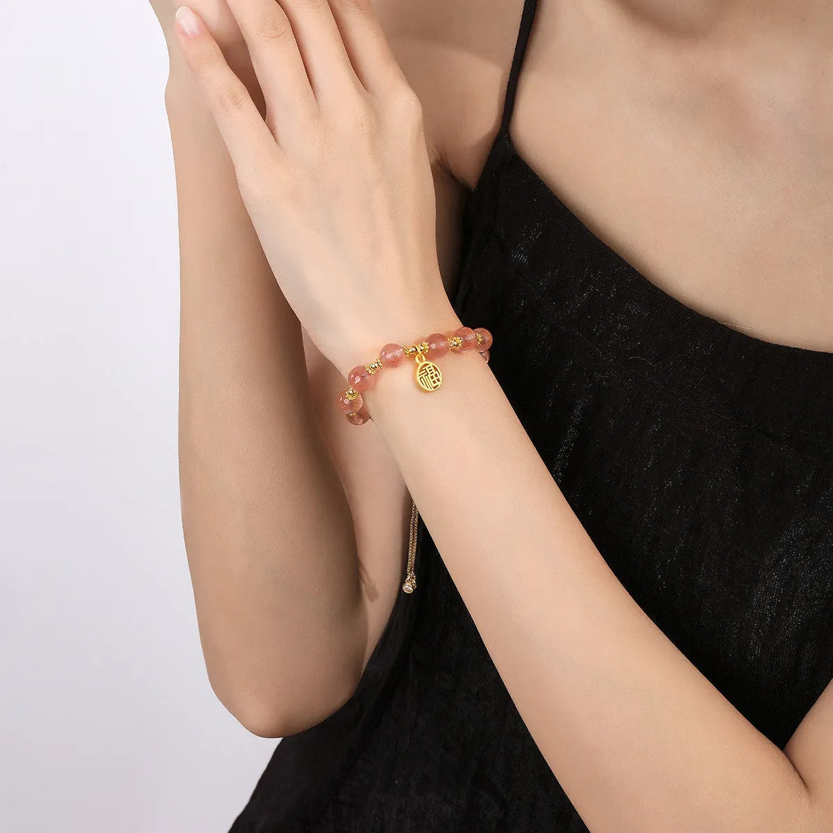 Close-up of a women's adjustable bracelet with pink strawberry quartz crystal beads and a silver fu charm on a geometric chain.