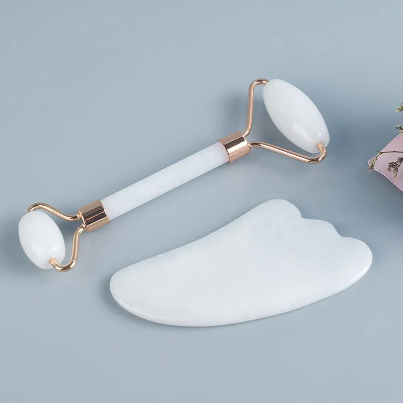 White jade facial roller and gua sha tool set with rose quartz board on a neutral background.