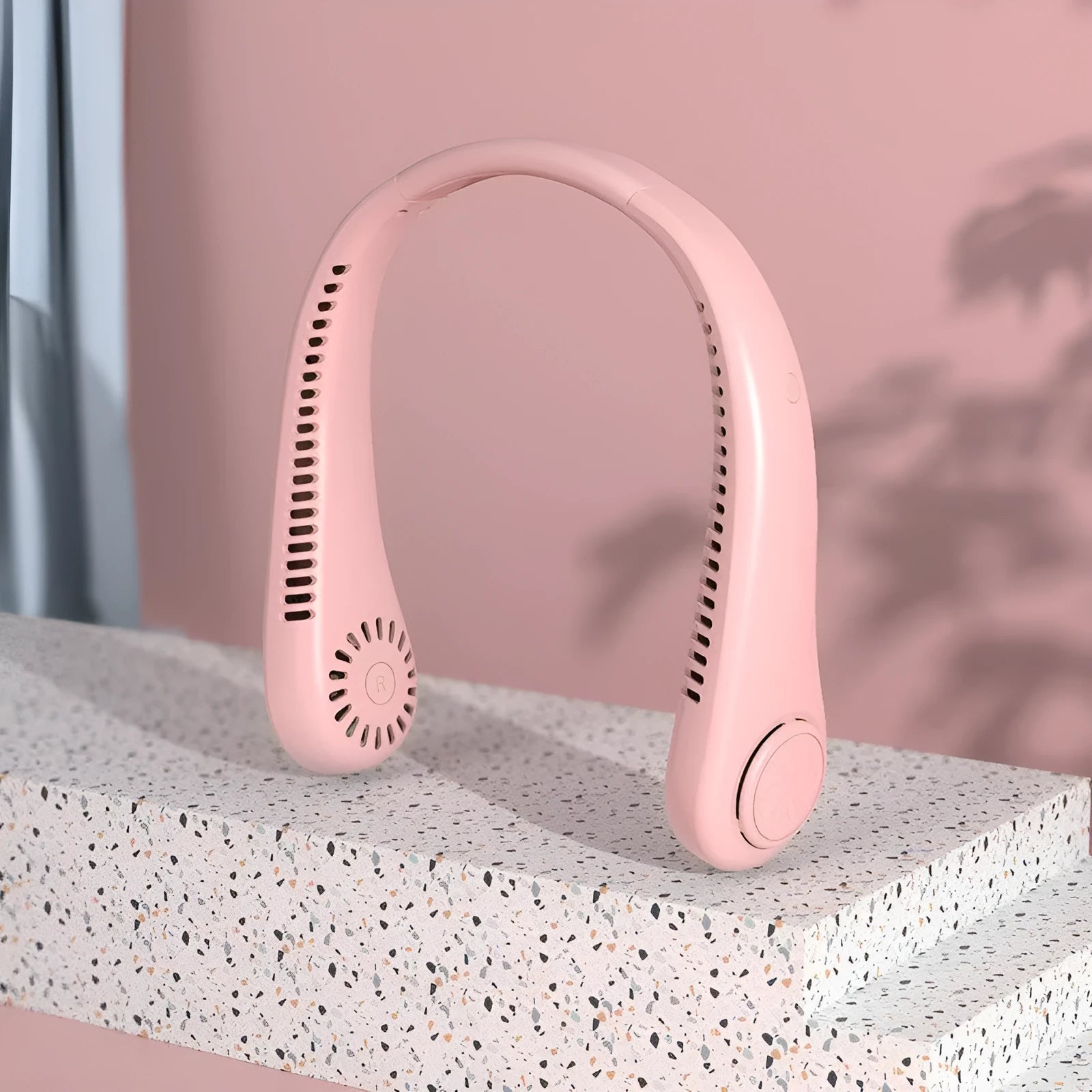 A pink bladeless neck fan hanging around a person's neck, showing its compact design and air outlets.