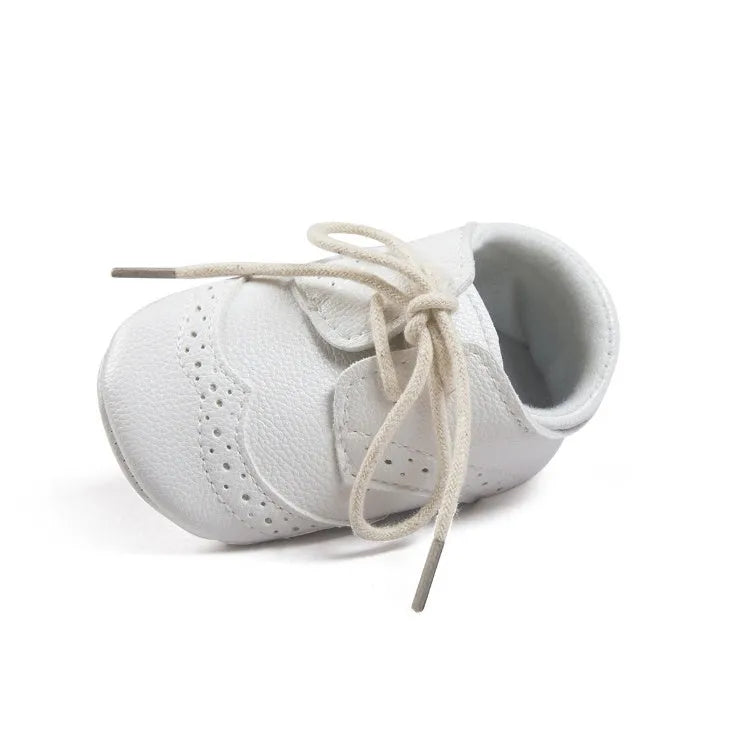 Vintage-style soft-soled baby shoes in black, grey, light brown, and white for infants 0-12 months.