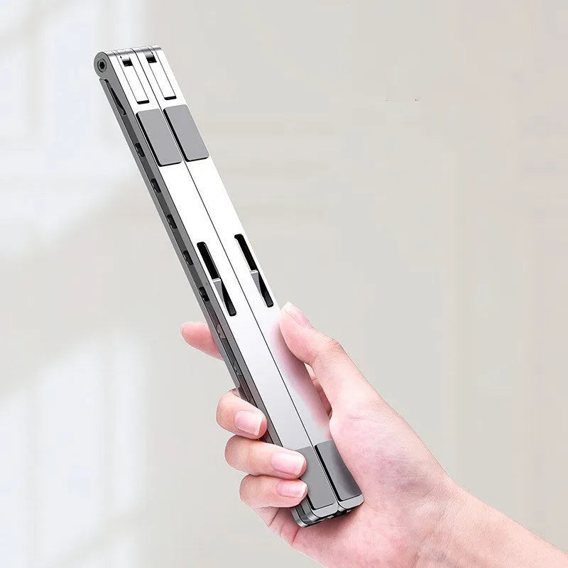 Folding flat aluminium alloy laptop bracket stand in silver with silicone pads, set at an angled position on a desk
