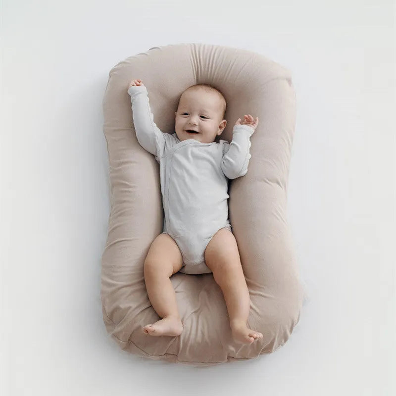 Cotton portable baby nest crib for newborns, beige colour, shown on a bed.