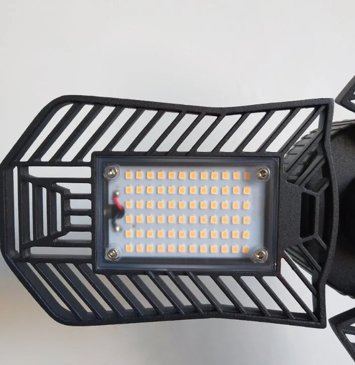 A foldable silver industrial LED garage lamp with a polycarbonate lens, shown in a workshop setting.