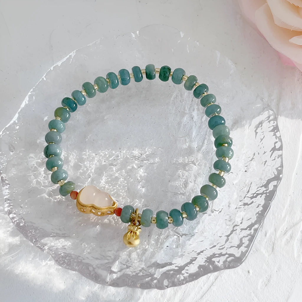 Close-up of a blue jade women's bracelet showing a gourd charm and a peace buckle charm on a string.