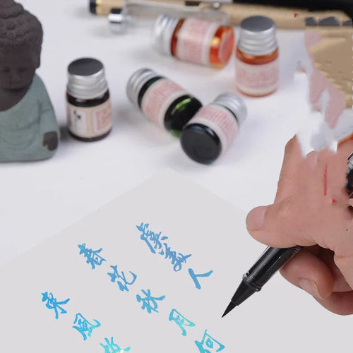 Set of six small glass bottles of pastel antiquity ink with gold powder for dipping pens.