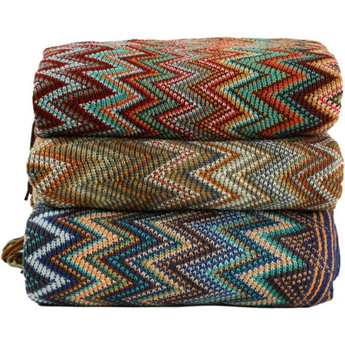Blue knitted acrylic blanket with striped pattern and fringe, draped over a sofa