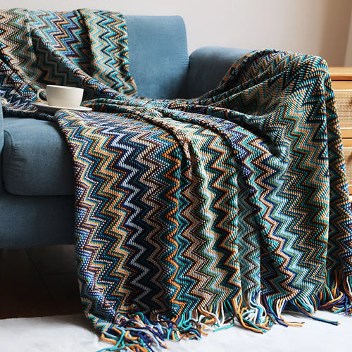 Blue knitted acrylic blanket with striped pattern and fringe, draped over a sofa