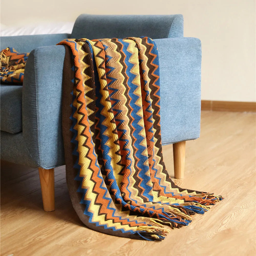 Blue knitted acrylic blanket with striped pattern and fringe, draped over a sofa